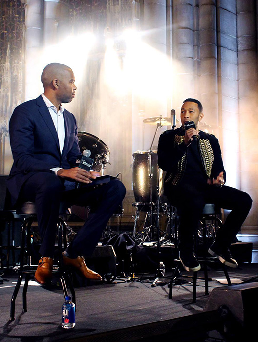 Singer John Legend sitting on stage talking into a microphone with host